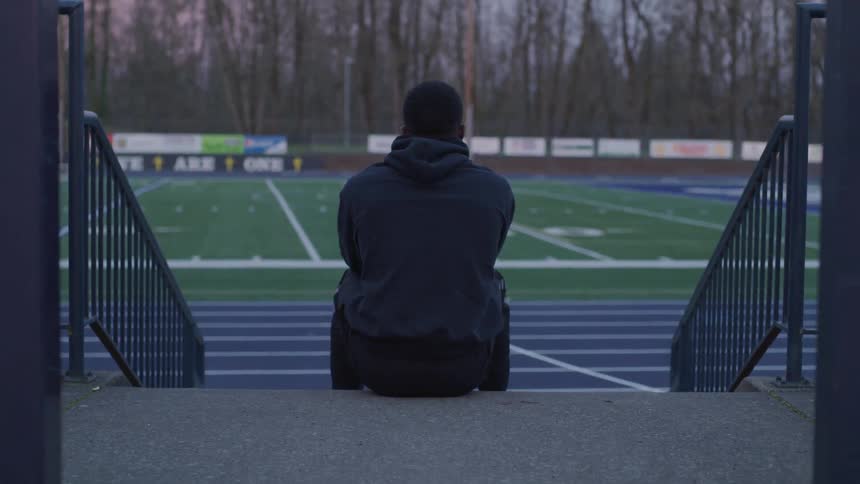 A man sitting on a staircase near an american football field