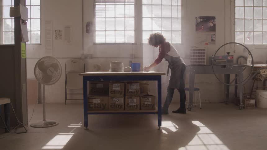 Man wearing apron kneads dough on the table while the sun streams through the window