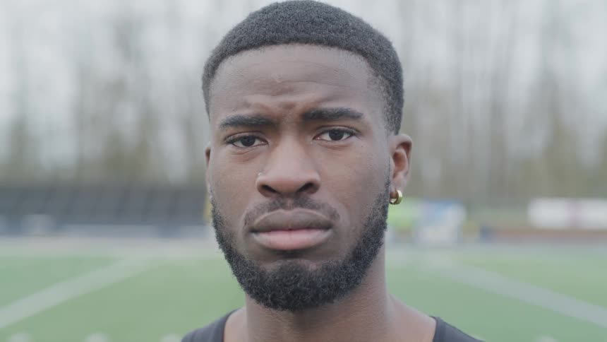 A black man standing before a football field looking towards the camera