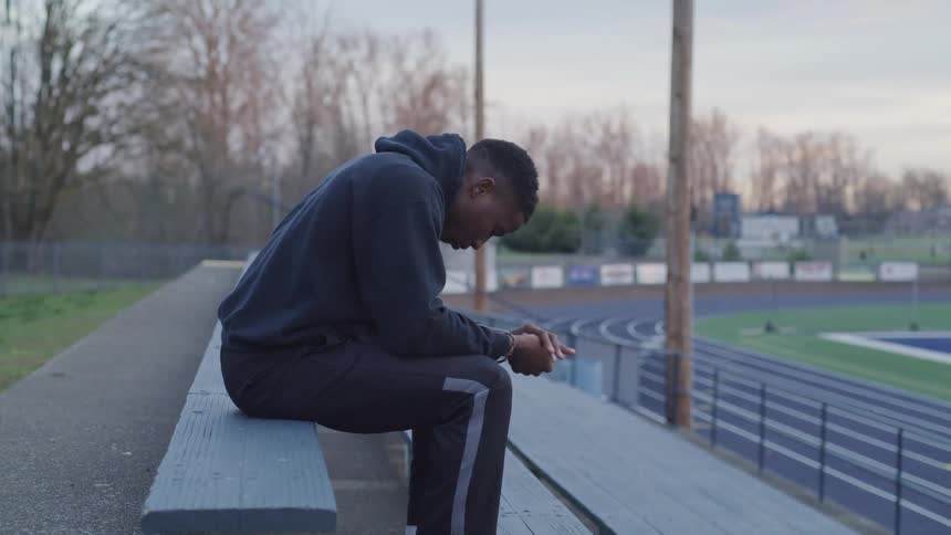 A man sits with his palms together on a bench