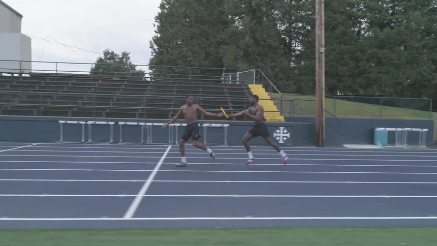 Male runners running on a track passing a baton