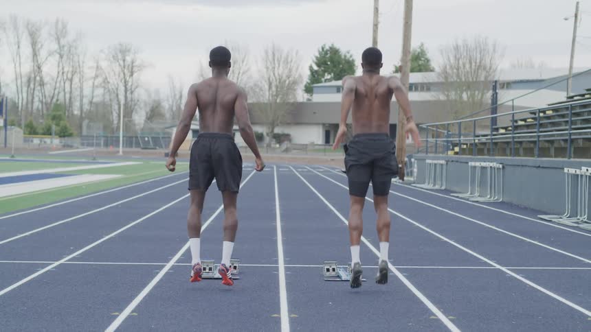 Two men jump up and down while standing on a track outdoors