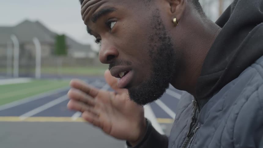 A man wipes his forehead standing on a running track