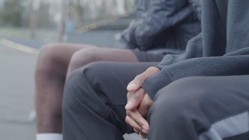 Two men in athletic gear sit side by side outside on a bench