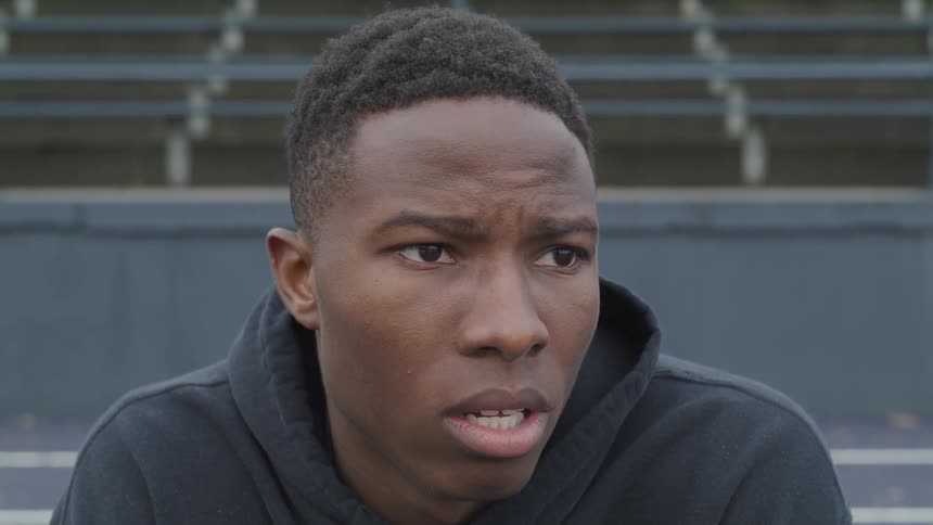 A young black man looks ahead and then drops his head down