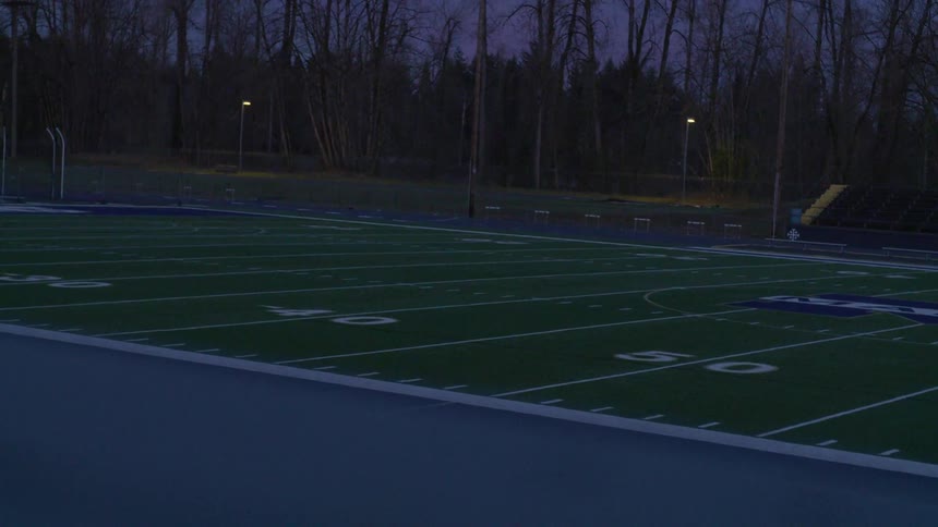 A football field sits empty amidst a forested area in the dark of night