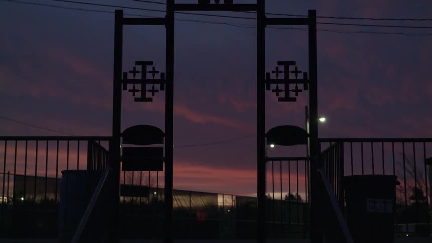 A fence and arch are silhouetted against a pink and blue sky at dusk