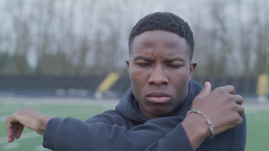 Man stands on football field staring grimly while stretching his shoulders