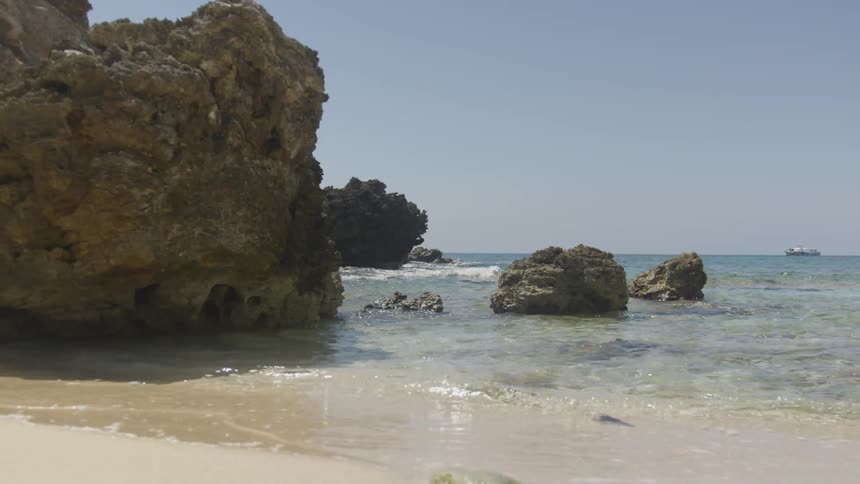 Waves crash into rocks and ripple on the beach sand