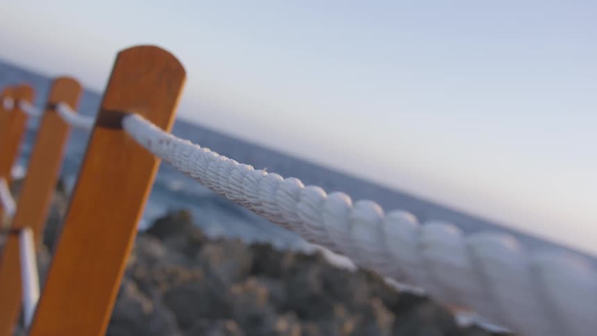 A rope fence with the ocean and a rocky shore in the background