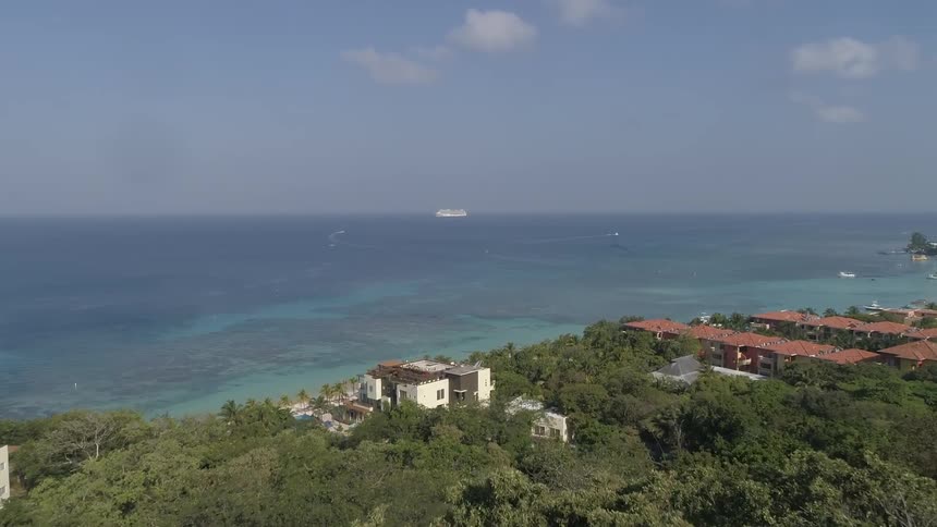 Passing over tree tops on a hill to the buildings and ocean coast below