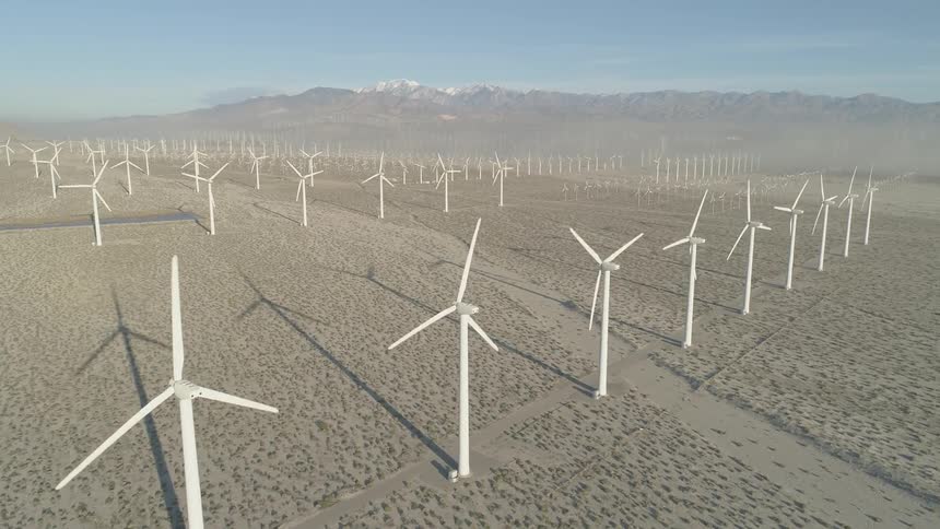 The blades of several wind mills in a flat wind mill farm are turning in the breeze