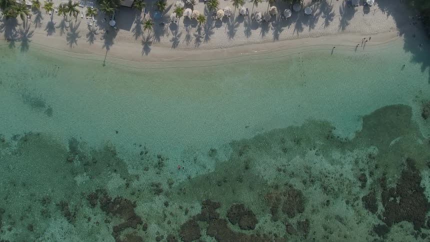 People walk on the tropical beach and wade in crystal clear ocean water
