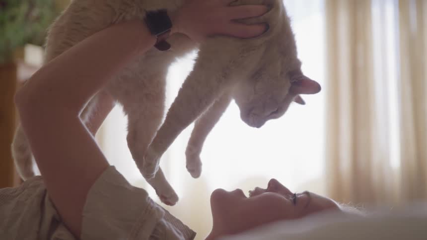 A woman that is laying in bed holding a cat over her face