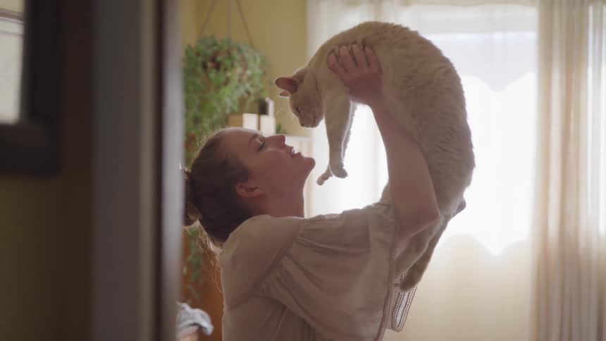 A young woman lifting and kissing a white cat
