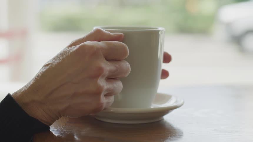 Hands holding a teacup on a table with a vehicle driving in the background