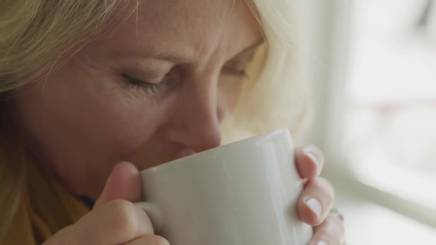 A woman drinks from a white mug