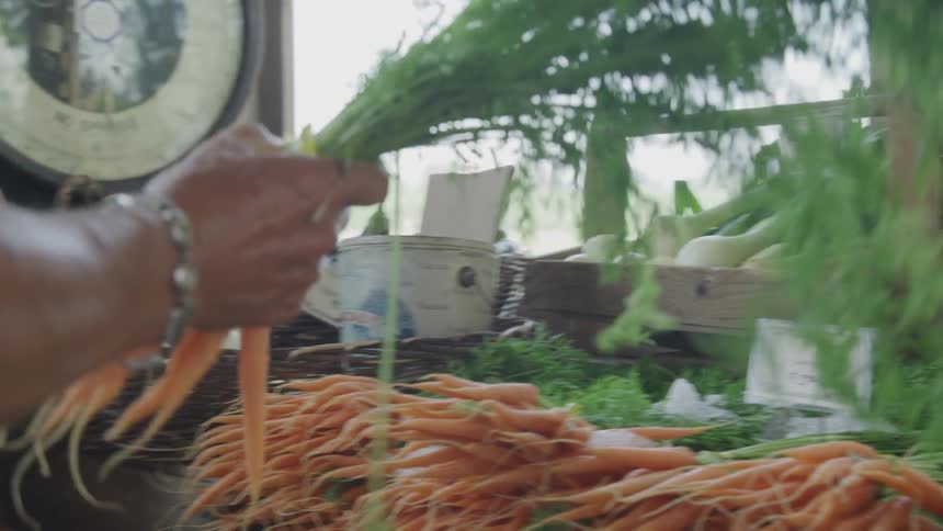 A woman reaches and grabs a bundle of carrots from a table