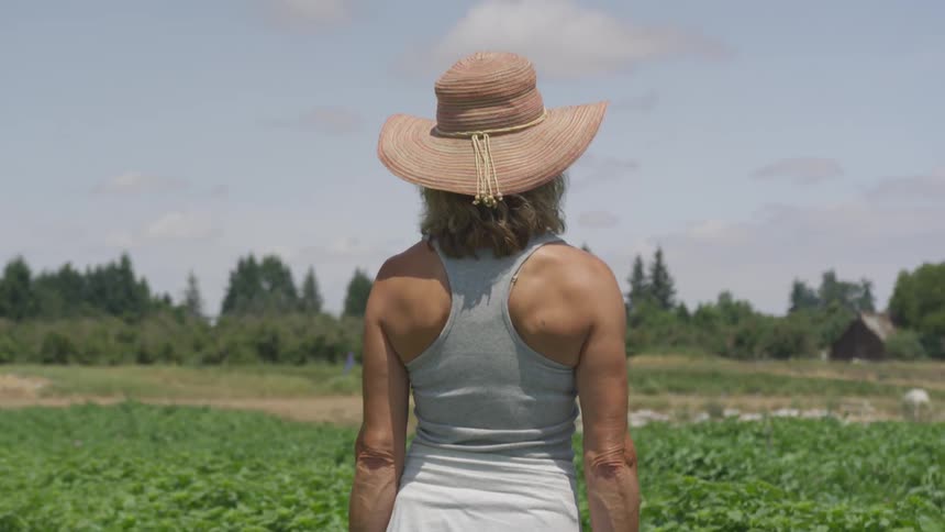 A woman stands outside looking across a field