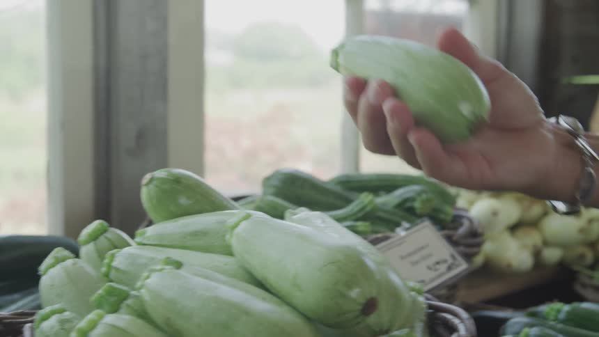 A woman picks up a vegetable and places it in a shopping basket