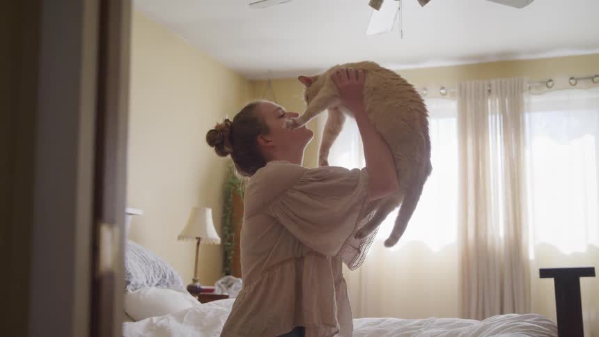 Girl lifting cat above head in room