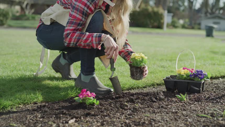 A woman uses a shovel to dig dirt for a flower plant