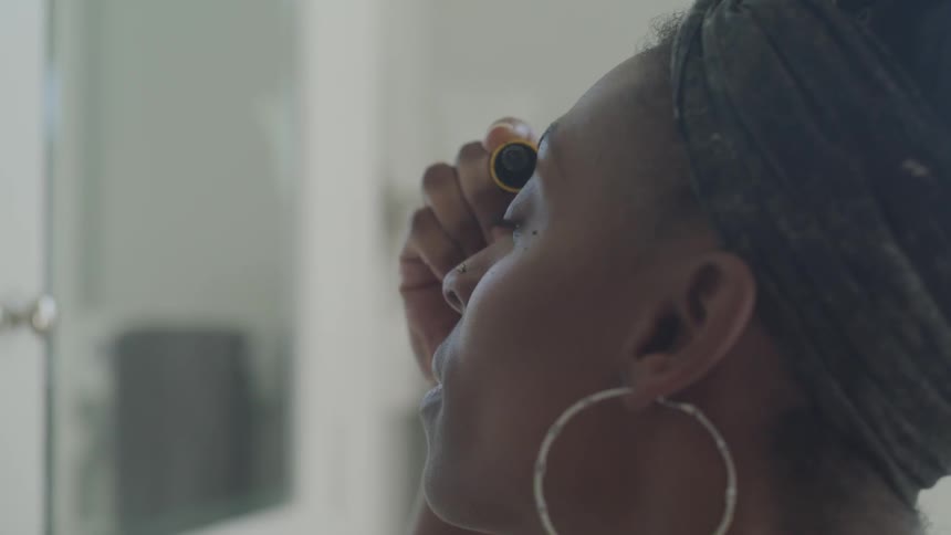 A black woman painting her eyelashes before a mirror