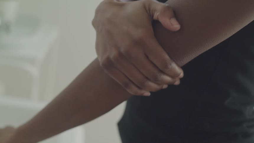 A black woman rubs her arm up to her elbow and back
