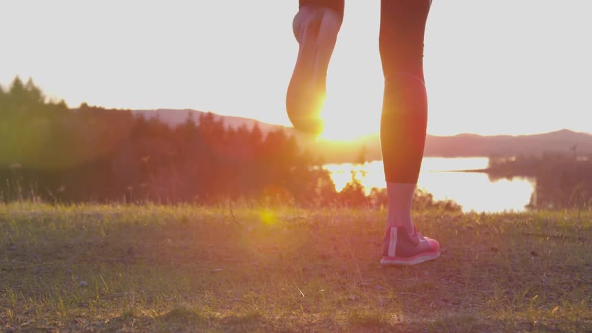 A woman stands at the top of a hill doing a warm up exercise during a sunset