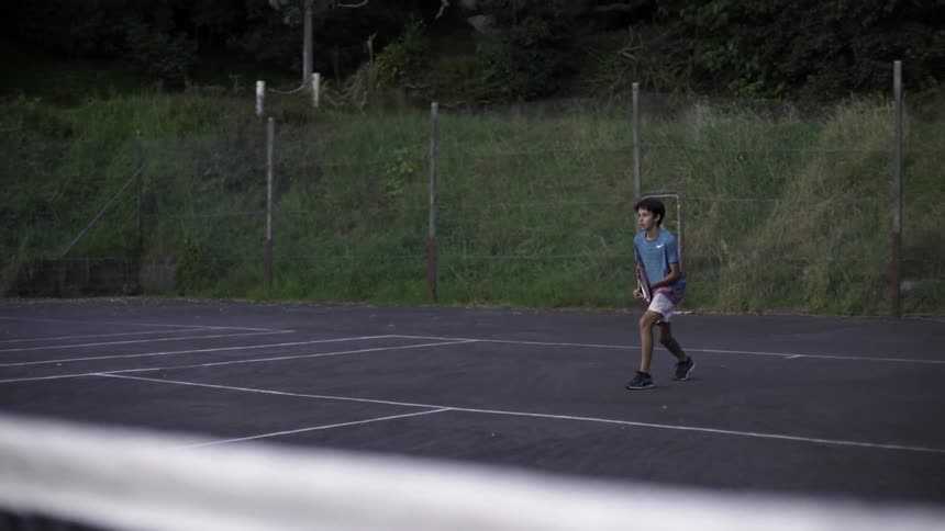 Young Boy Playing Tennis on Outdoor Court Under Bright Sunlight, Sports Clip.