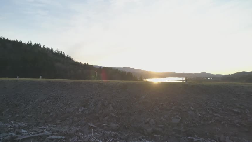 A woman slowly walks along a dirt trail next to a lake and mountain