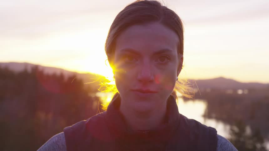 Portrait of a woman standing on a snowy mountain side with a sunset in the background