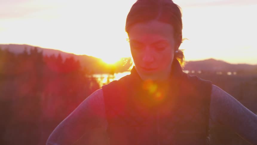 Woman stands in the forest while the sun goes down