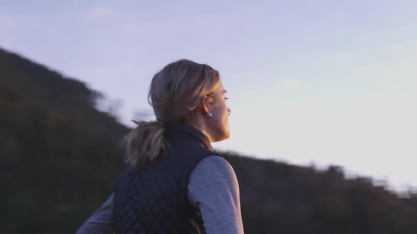 Blonde woman breathes and looks at the sunset at the base of the mountain