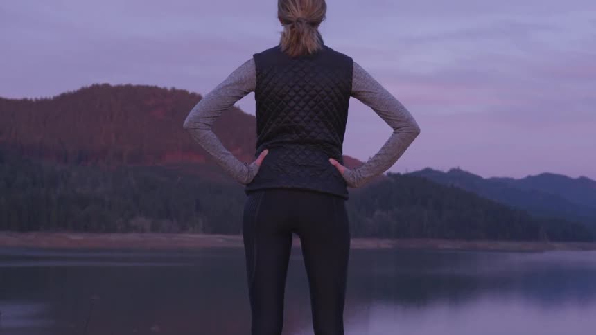 A woman stands and looks towards a lake