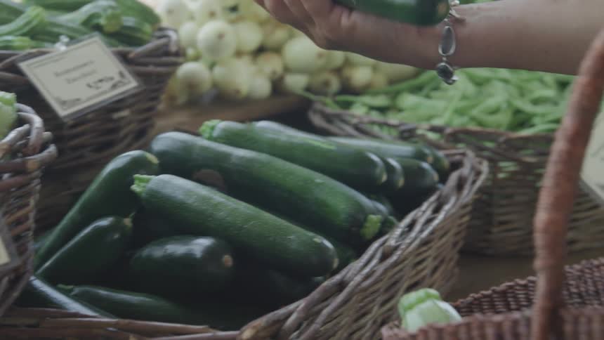 A woman picks up a cucumber and places it in a shopping bag
