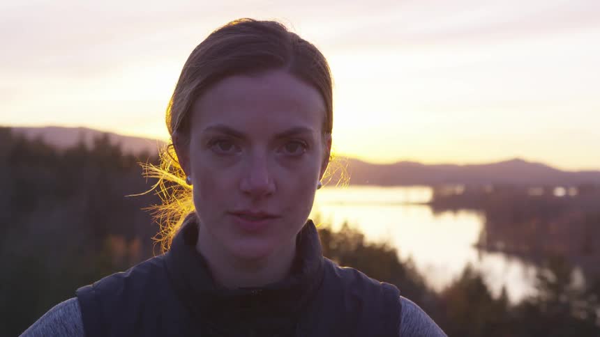 A woman with her hair tied back looks down a camera at sunset