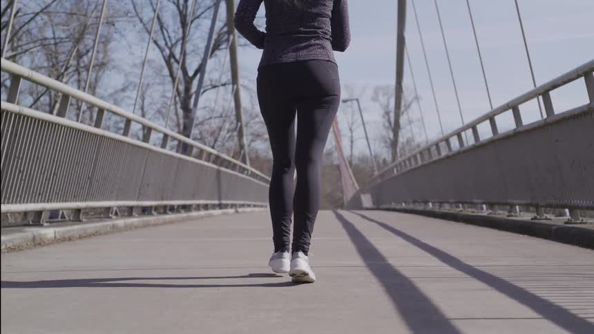 Woman in black leggings and white sneakers jogs across a concrete bridge