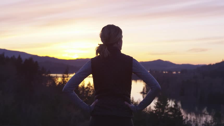A woman is standing outdoors looking at the sunset