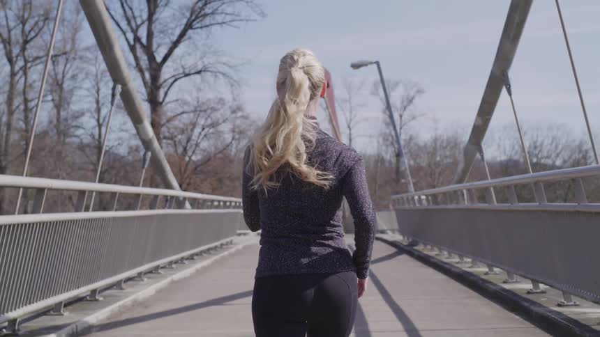 Woman jogging across a bridge at sunny day