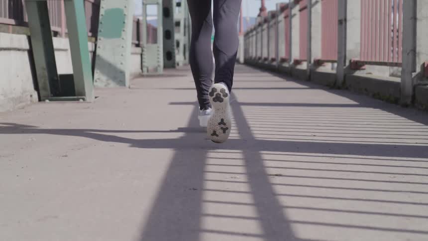 The soles of a joggers sneakers are visible as they jog across a pedestrian bridge on a sunny day