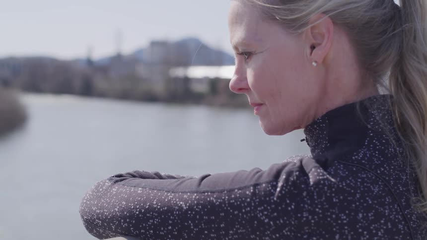 A blonde woman sits next to a river