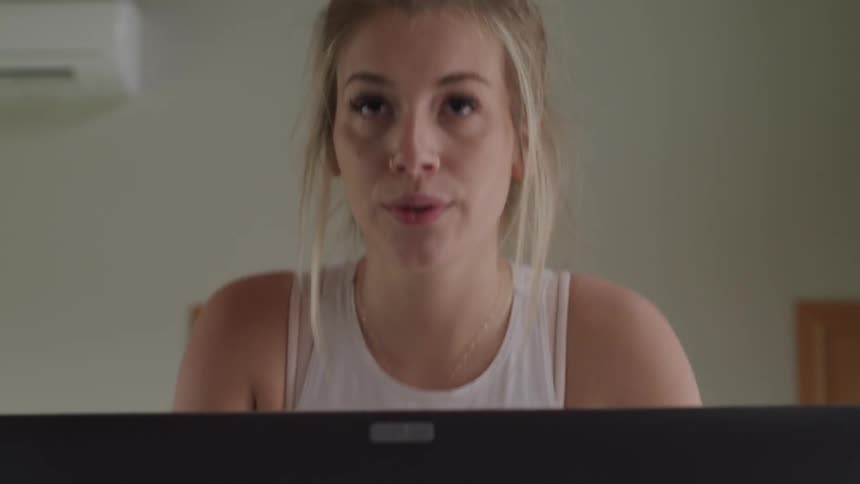A young blonde woman in a tank top is exercising on a piece of equipment