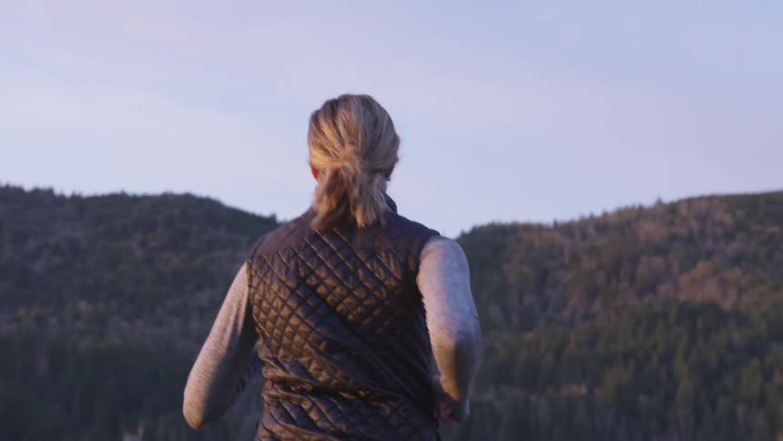 A woman jogs towards a forest on a clear day
