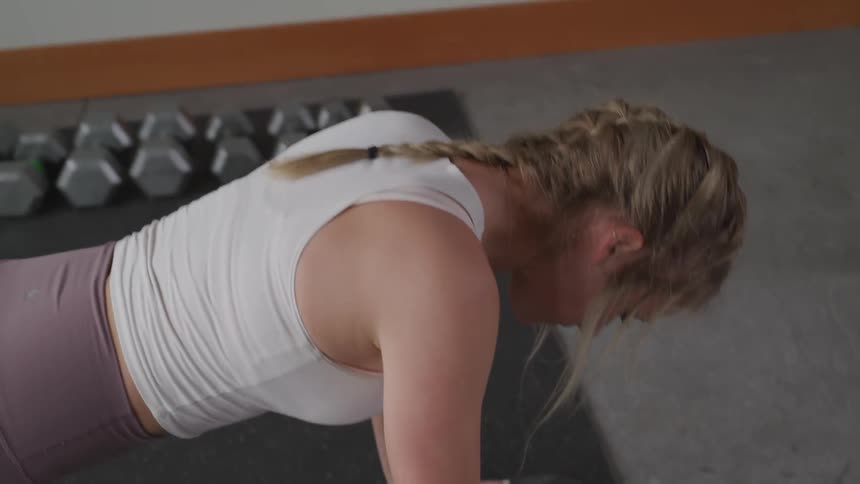 Blonde woman wearing white tank top doing push up at the gym