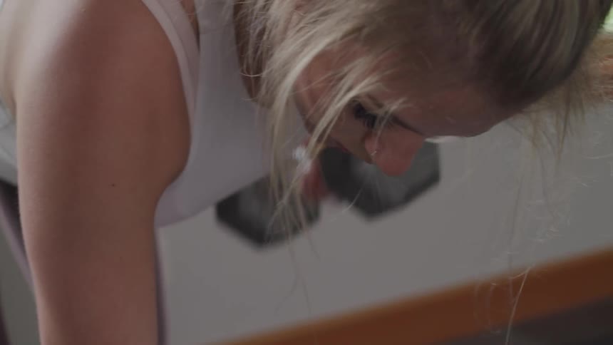 A woman in a sports vest and yoga pants lifts weights in a bright room
