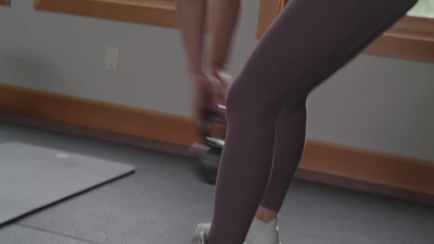A young woman with plaited hair and wearing yoga pants works out indoors