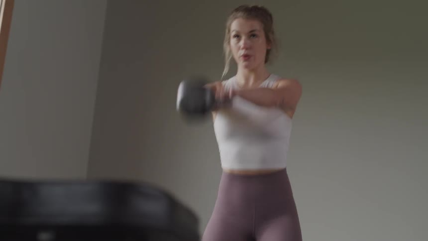 Blonde woman lifts kettlebell indoors during daylight