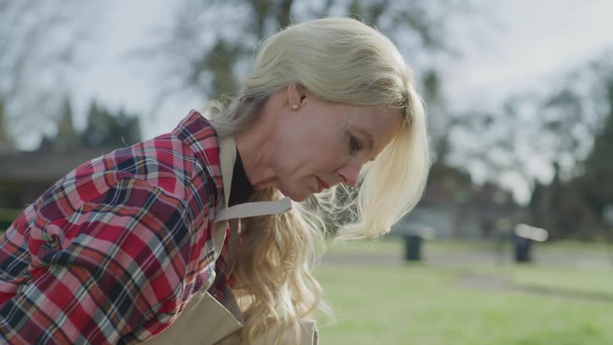 A woman doing gardening while wearing a tan apron