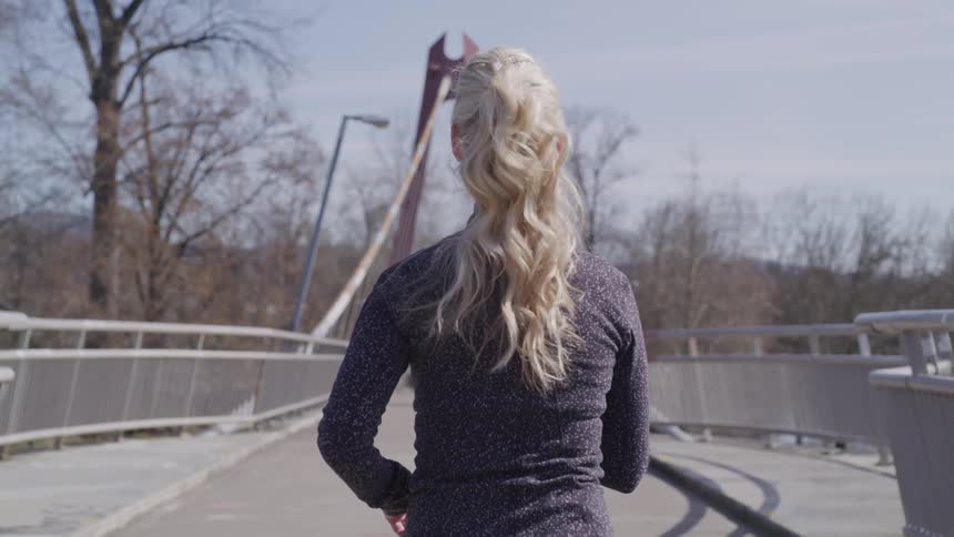 Woman power walks towards a bridge under a sunny sky